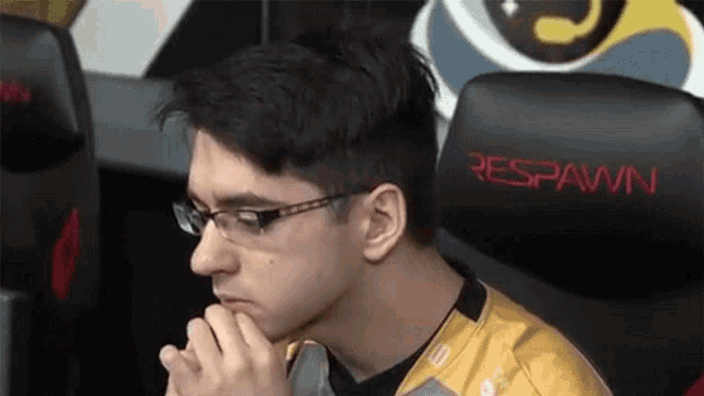 a man wearing glasses is sitting in a chair that says respawn on it