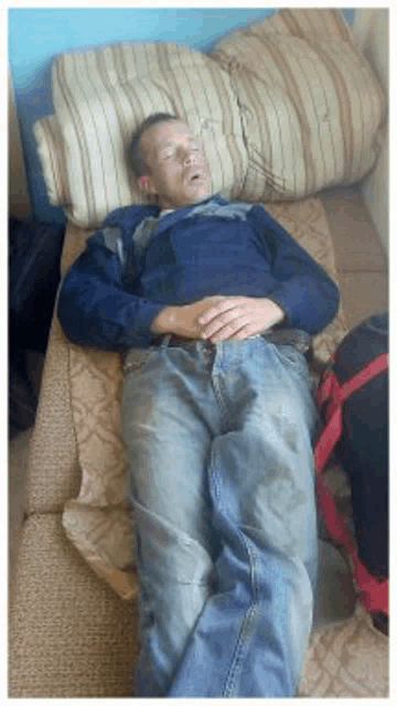 a man in a blue shirt and jeans is sleeping on a bed