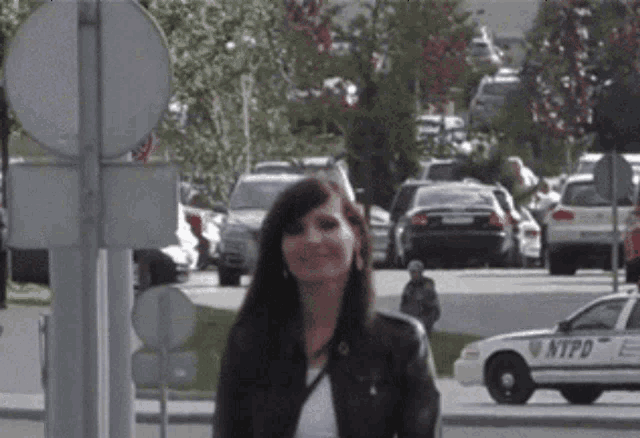 a woman walking down a street next to a nypd car