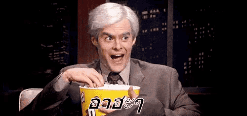 a man in a suit is eating popcorn from a yellow bucket