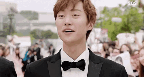 a young man in a tuxedo and bow tie is standing in front of a crowd .