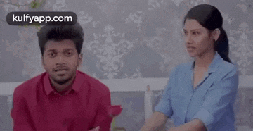 a man and a woman are sitting next to each other on a couch and the woman is pointing at the man .