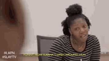 a woman in a striped shirt is sitting at a table and making a face .