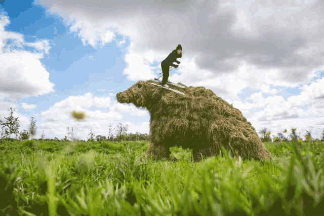 a person standing on top of a pile of hay in the shape of a bear