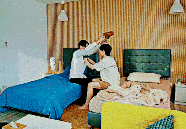 two men are playing with each other in a bedroom with striped walls and a bed with a blue comforter