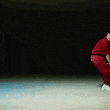 a group of people are standing in a dark room and one of them is wearing a red jumpsuit
