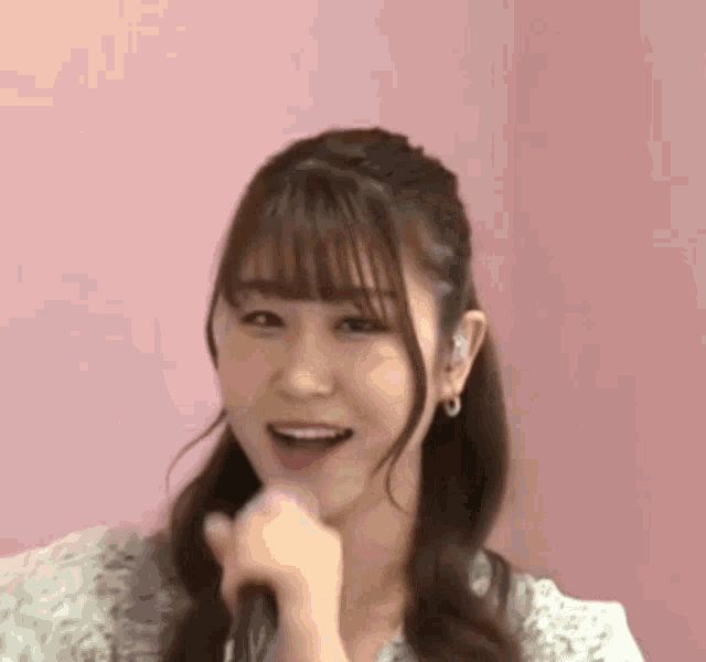 a woman is singing into a microphone and smiling while standing in front of a pink wall .