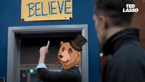 a man with a bear head pointing at a sign that says believe