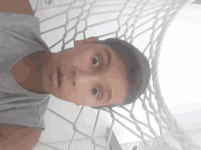 a young boy is laying in a hammock and looking at the camera with a surprised look on his face