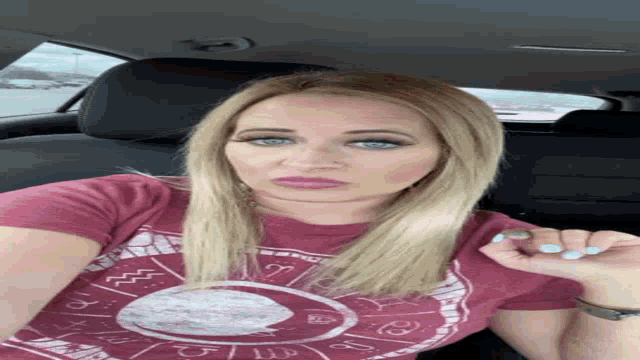 a woman in a car wearing a red shirt with a zodiac sign on it