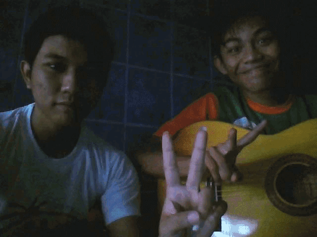 a man giving a peace sign while another man holds a guitar