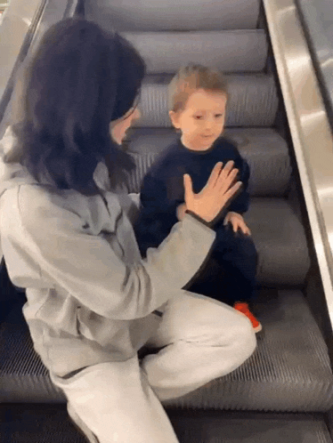 a woman is sitting on an escalator talking to a little boy