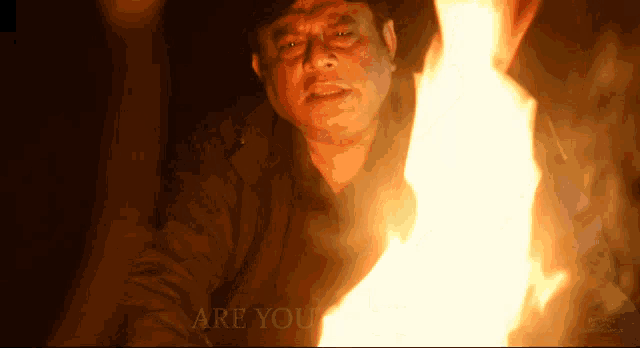 a man standing in front of a fire with the words " are you " written below him