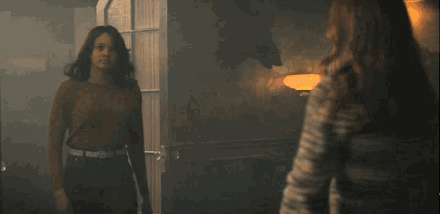 three women are standing next to each other in a dark room with a lamp in the background