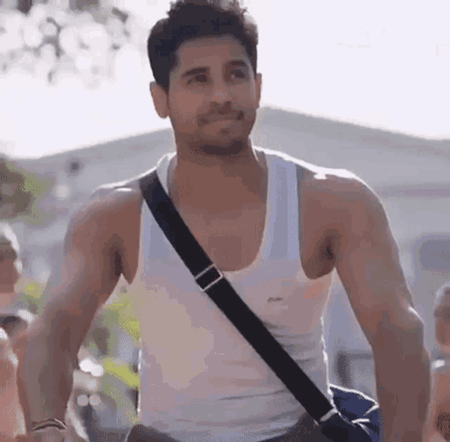 a man in a white tank top is walking down the street with a blue bag .