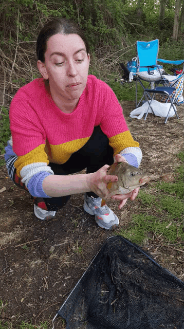 a woman in a pink sweater is holding a small fish