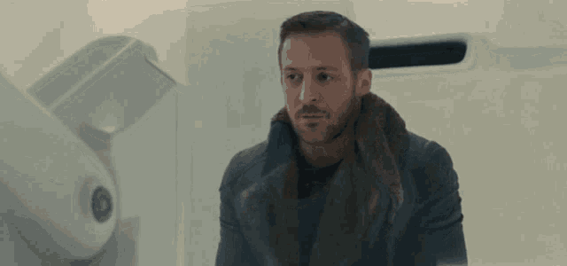 a man with a beard is sitting in a bathroom with a white wall .
