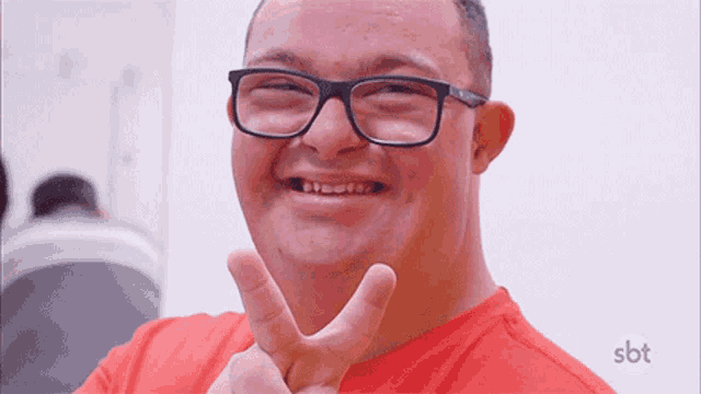 a man wearing glasses and a red shirt is smiling and making a peace sign