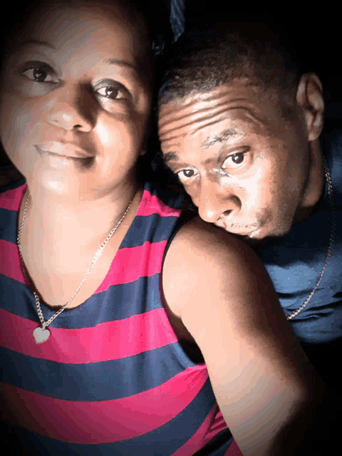 a man and woman are posing for a picture and the woman has a heart necklace