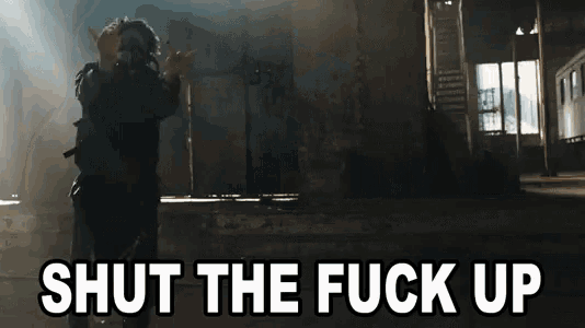 a man wearing a gas mask is standing in front of a sign that says shut the fuck up .