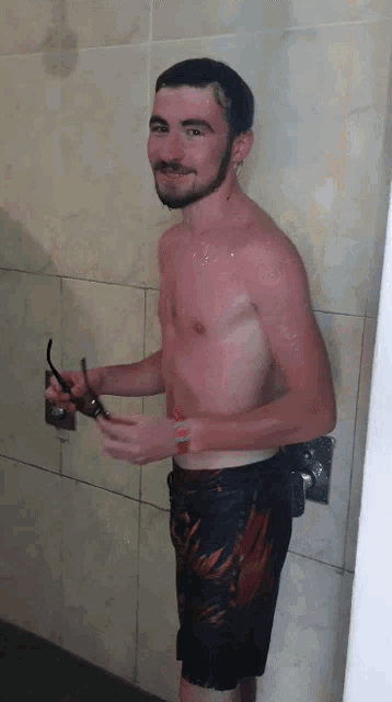 a shirtless man is standing in a shower holding sunglasses