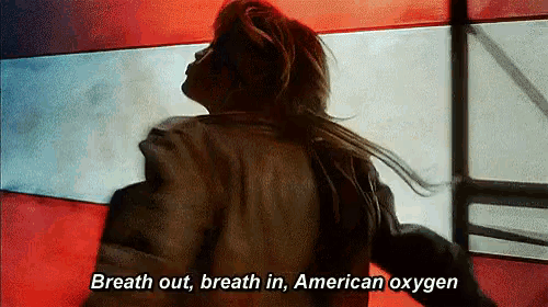 a woman in a leather jacket is standing in front of an american flag and says breath out breath in american oxygen .