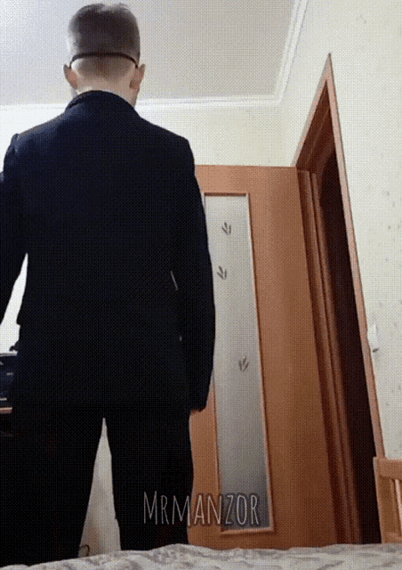 a man in a suit is standing in front of a door with the name mrmanzor written on it