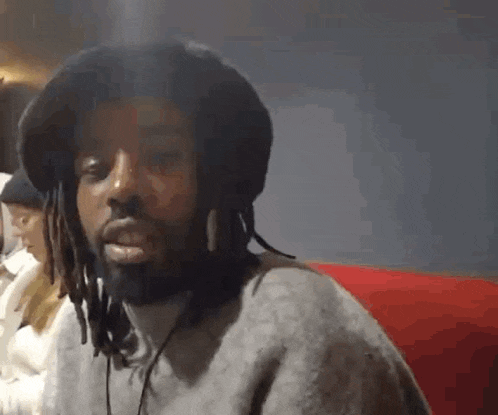 a man with dreadlocks and a beard is wearing a hat and headphones .