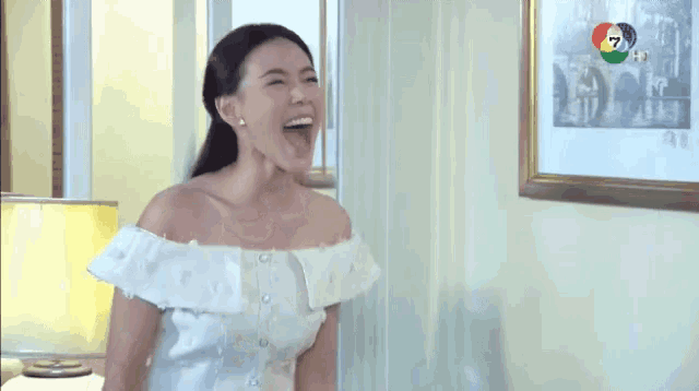 a woman in a white off the shoulder dress is laughing in a room with a picture on the wall .