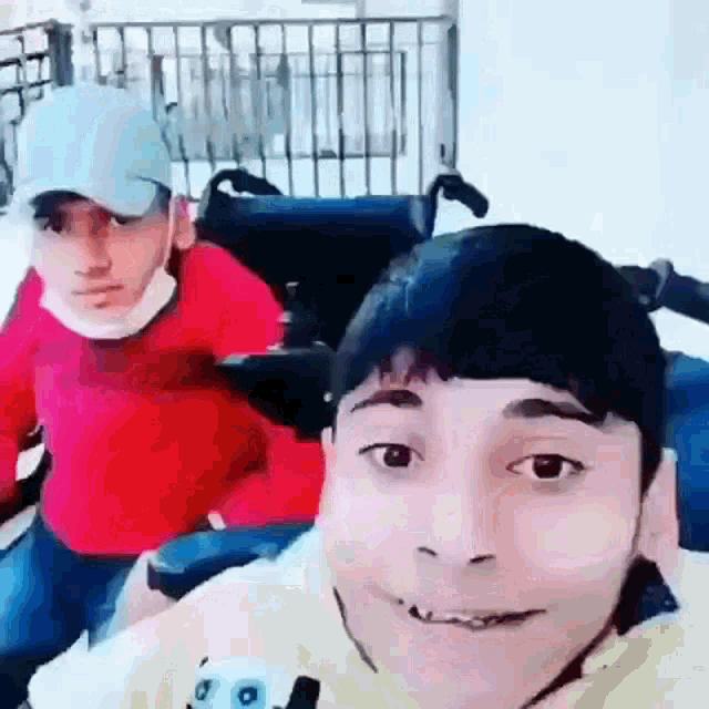 a man in a wheelchair is sitting next to another man in a red sweater .