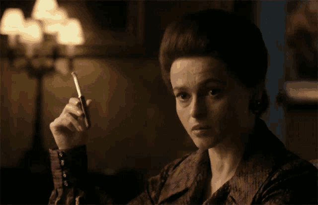 a woman in a purple shirt is smoking a cigarette in a dark room