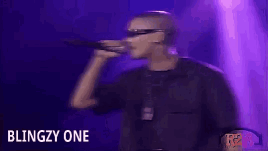 a man is singing into a microphone with the words blingzy one behind him