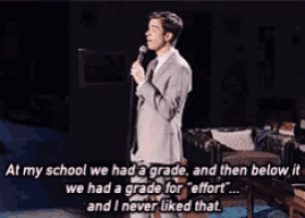 a man in a suit and tie is speaking into a microphone and says " in my school we had a grade "