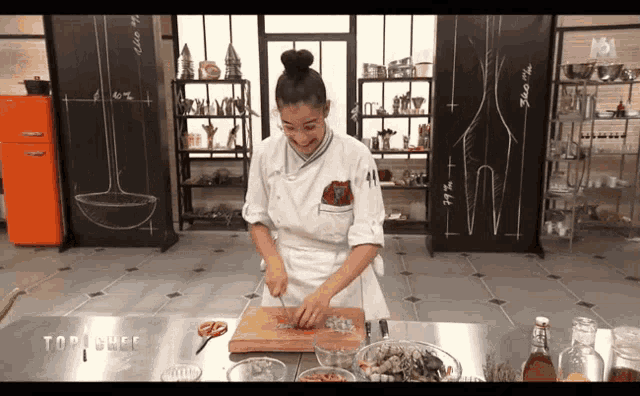 a woman in a chef 's uniform is cutting vegetables on a cutting board in front of a sign that says top chef
