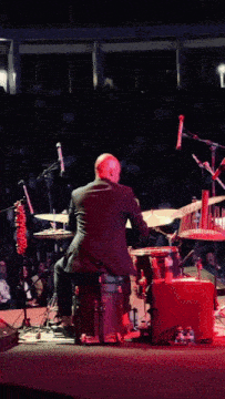 a man is playing drums on a stage with a crowd watching
