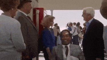 a group of people are standing around a man in a suit and tie