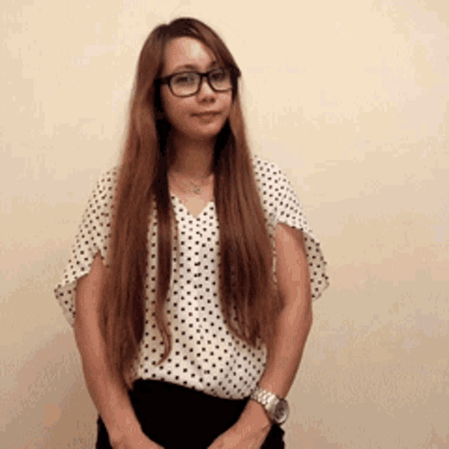 a woman wearing glasses and a polka dot shirt stands in front of a wall