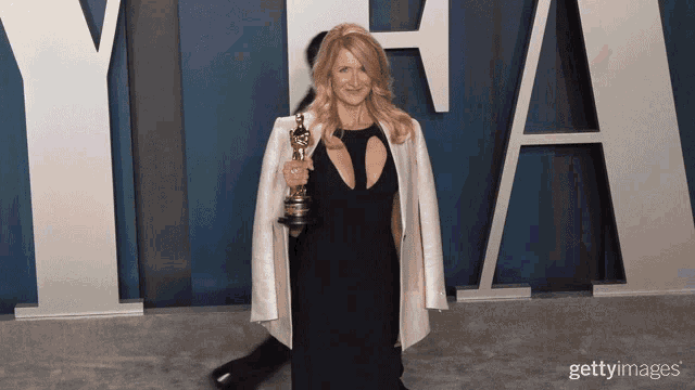 a woman in a black dress is holding an oscar statue