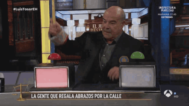 a man in a suit stands in front of a screen that says la gente que regala abrazos por la calle on it