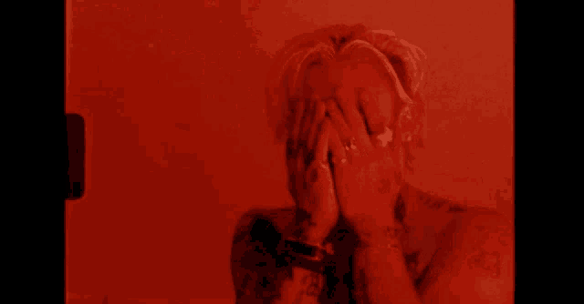 a shirtless man with tattoos is covering his mouth with his hands .