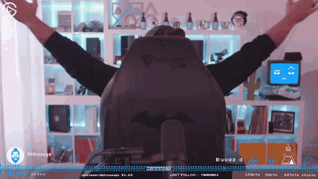 a man is sitting in a gaming chair with his arms outstretched in front of a bookshelf