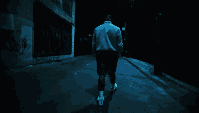 a person is walking down a dark street with graffiti on the wall
