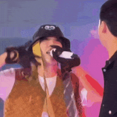 a man is drinking from a bottle while wearing a hat with googly eyes