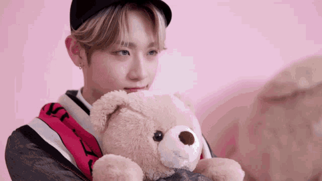 a young man is holding a teddy bear in his arms with a pink background