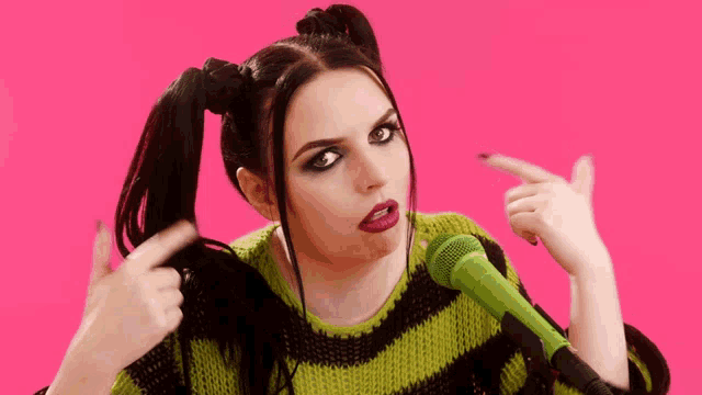 a woman in a green and black striped sweater is singing into a microphone
