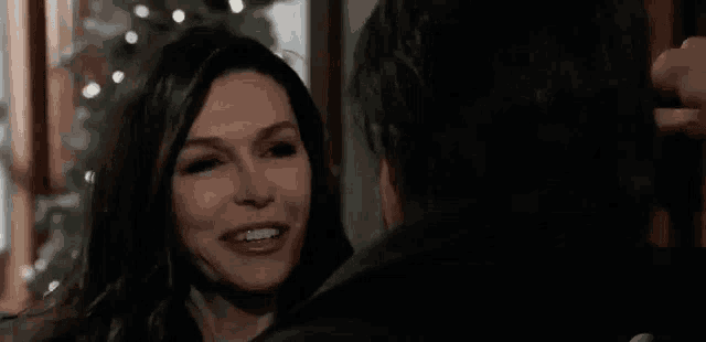 a woman is smiling at a man in front of a christmas tree while they are looking at each other .