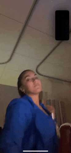 a woman in a blue shirt is standing in a room with a phone in the background .