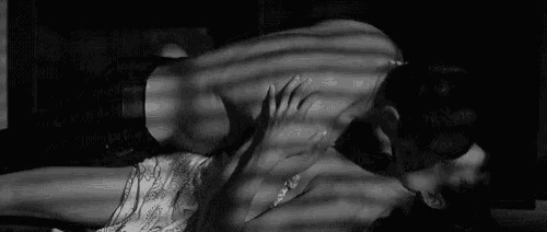 a man and a woman are kissing while laying on a bed in a black and white photo .
