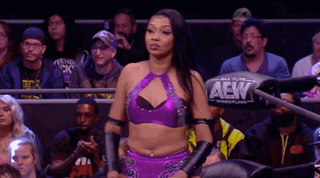 a woman in a purple wrestling outfit is standing in front of a crowd of people .