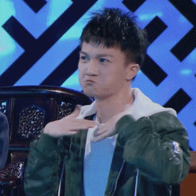 a young man in a green jacket making a face